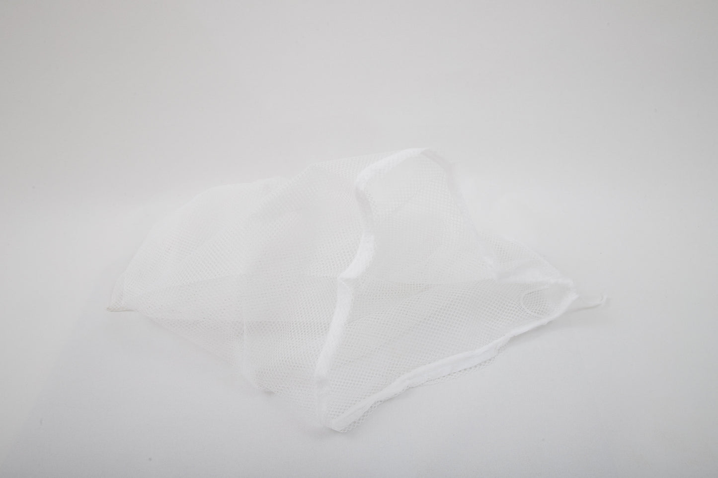 A Laundry Washing Bag made of white mesh fabric lies crumpled on a plain white background.