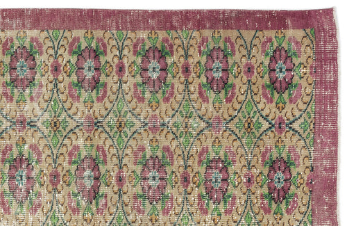 Load image 1 in gallery view. Distressed beige rug with a magenta border and a repeating floral medallion pattern in magenta, green, and teal.