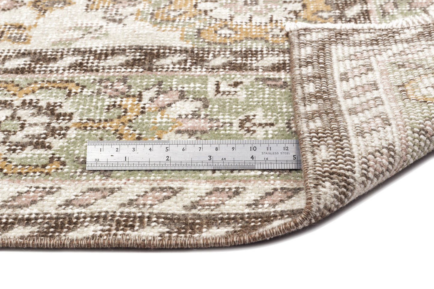 A close-up of the Nizora - Vintage Floral Rug (6'1 x 10'0) shows a metal ruler in inches and centimeters on top, with one corner folded to display the underside.