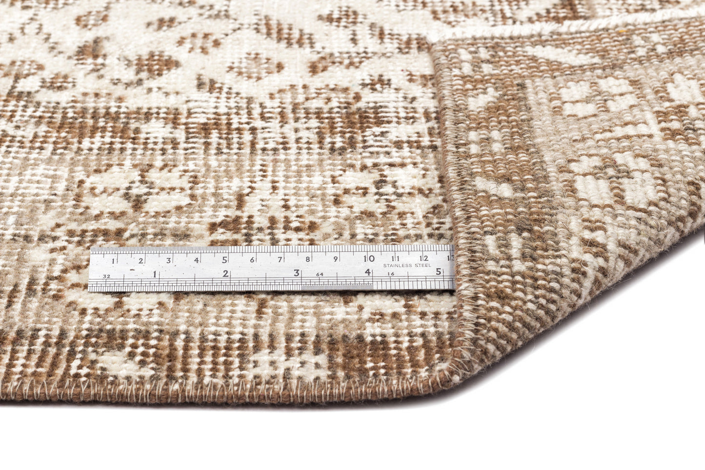 Brown and cream distressed patterned rug with a folded corner and a metal ruler for scale.
