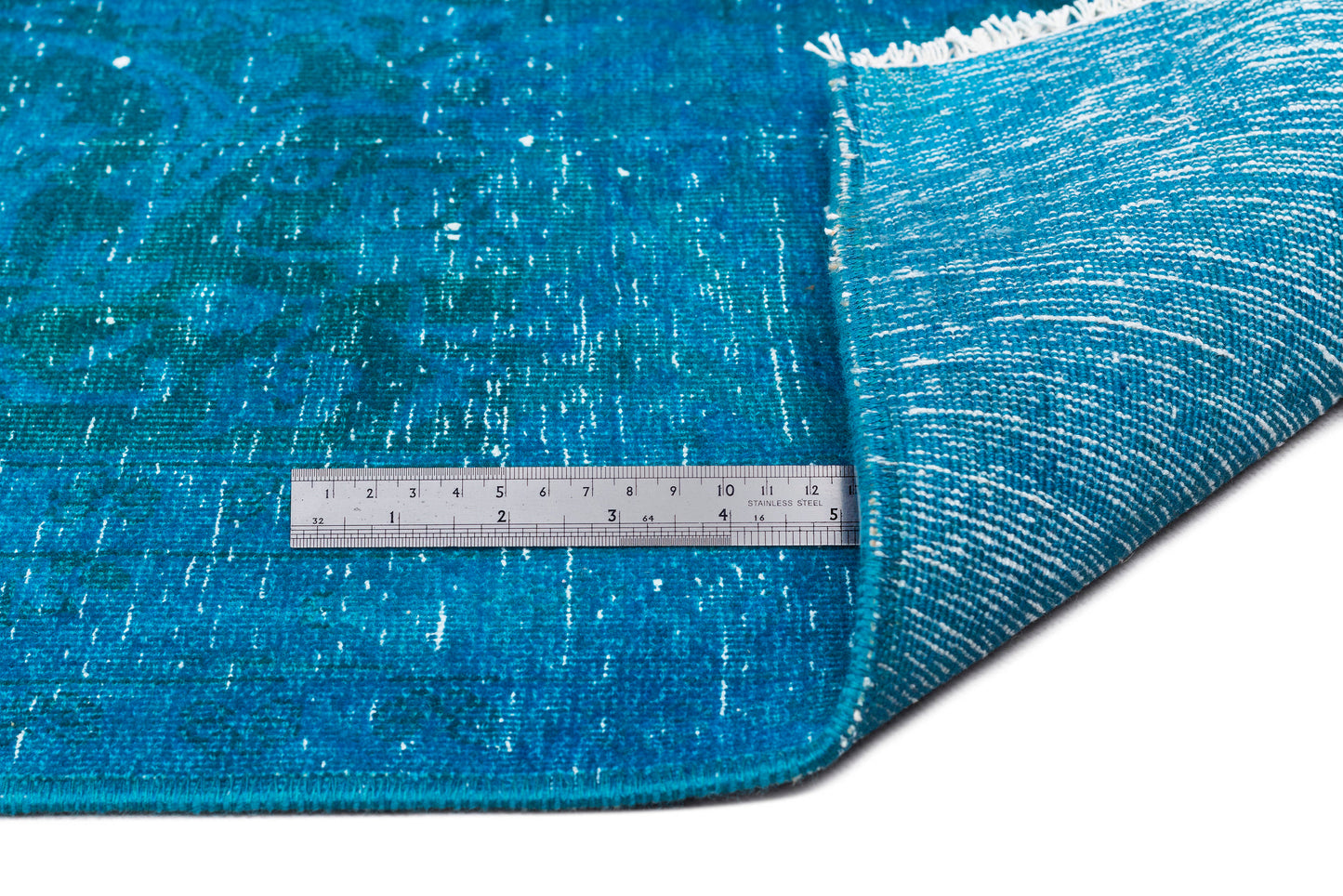 Distressed teal rug with a faded traditional pattern, white fringe, and a metal ruler for scale on a white background.