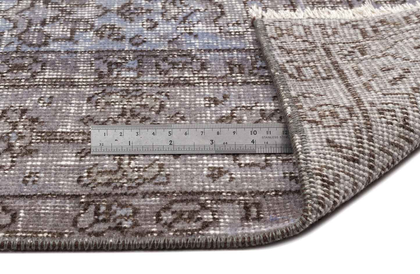 Blue and brown distressed traditional rug with a folded corner and a metal ruler for scale on a white background.