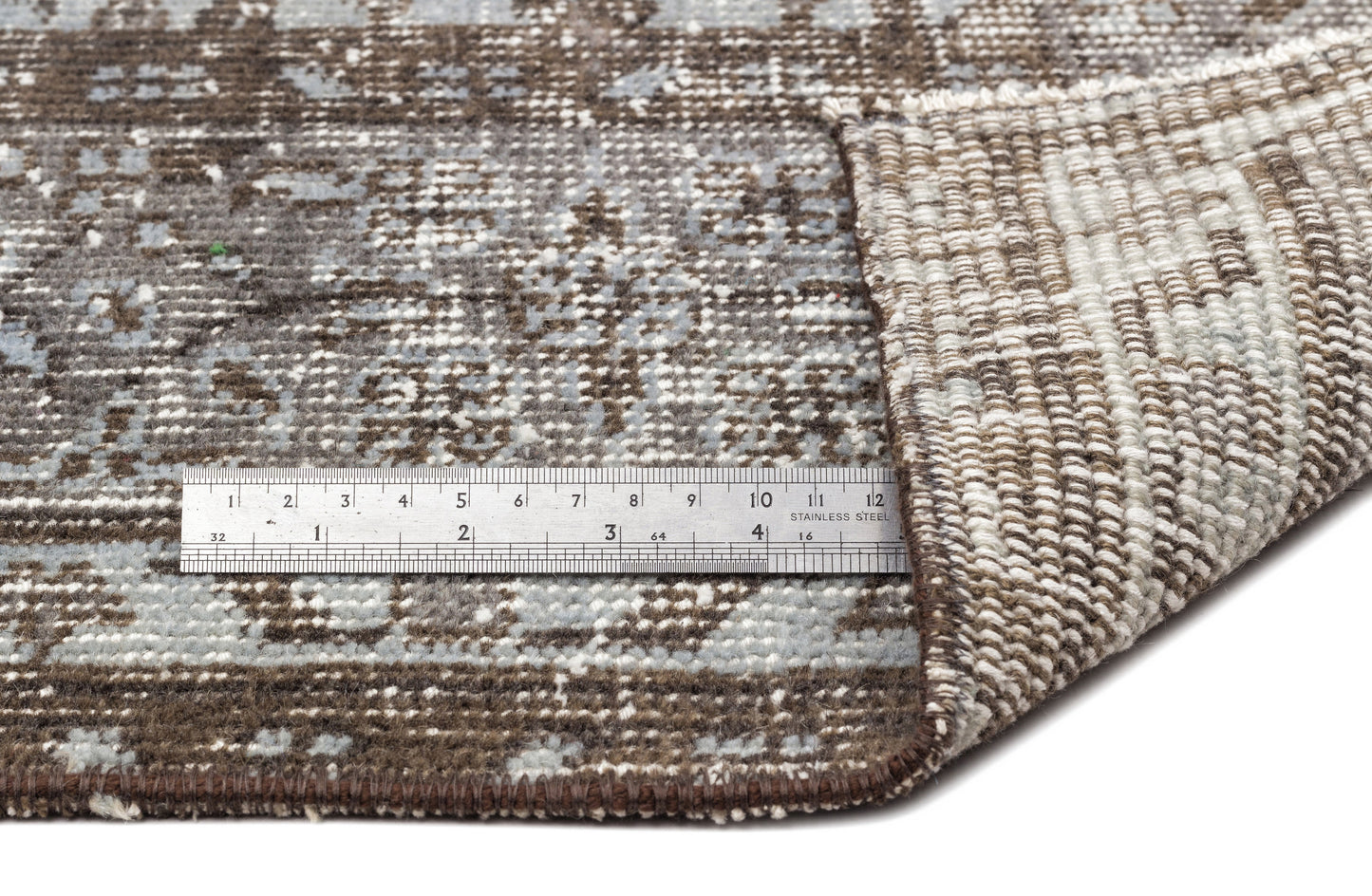Brown and grey distressed pattern rug with a folded corner and a metal ruler for scale.