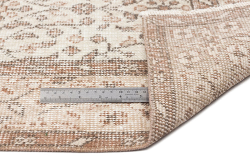 Load image 1 in gallery view. A close-up of the Pavia - Vintage Floral Rug (5'7 x 9'5) in beige and brown, with one corner folded over, next to a metal ruler showing inch and centimeter measurements for scale.