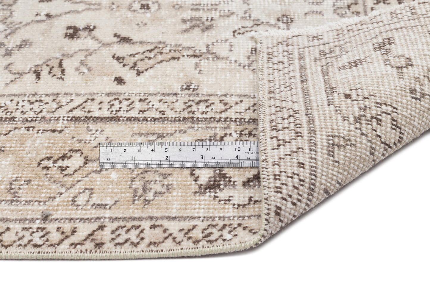 Beige and brown distressed traditional rug with a folded corner and a metal ruler for scale on a white background.