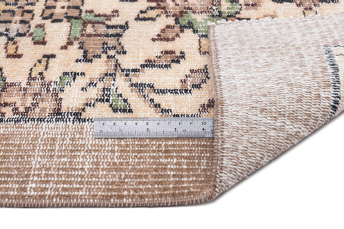 Load image 1 in gallery view. Beige rug with a distressed floral pattern and a metal ruler showing pile height, folded corner revealing the backing.