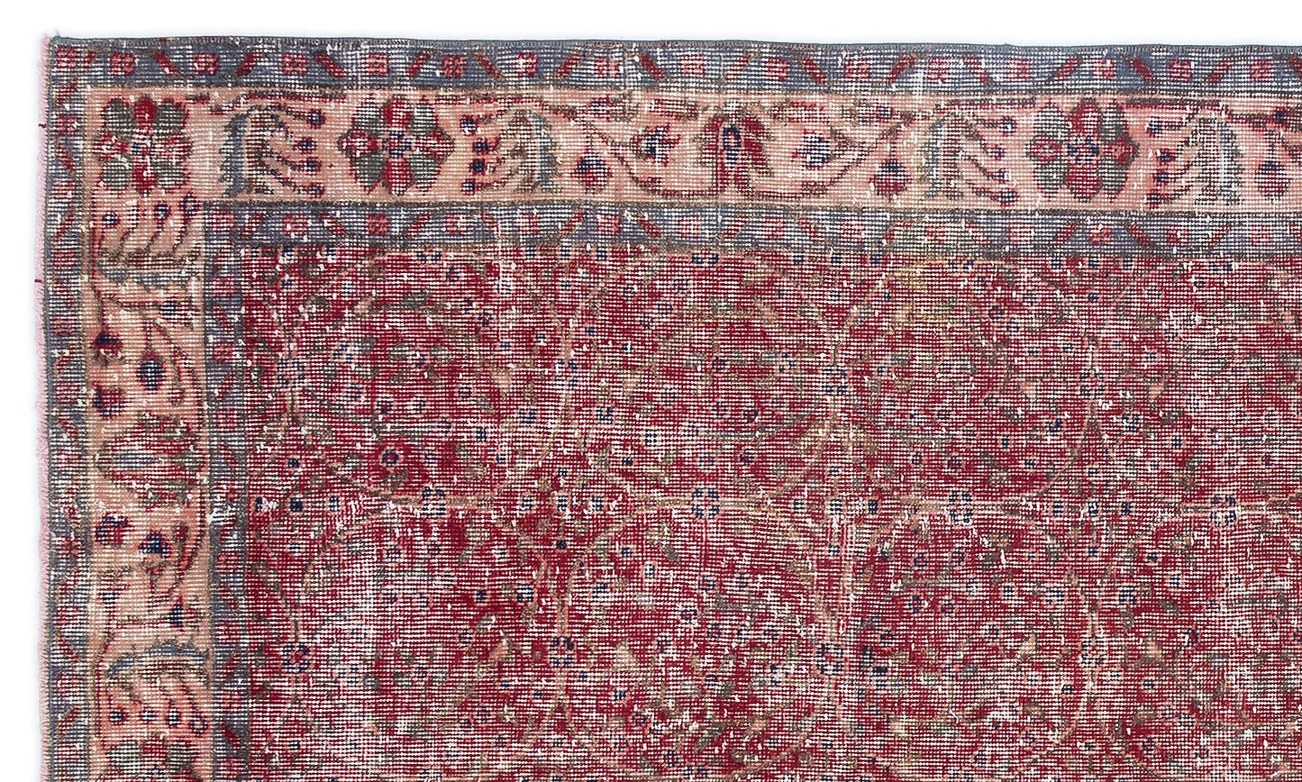 Distressed red rug with a faded floral border and a repeating geometric medallion pattern in blue and cream.