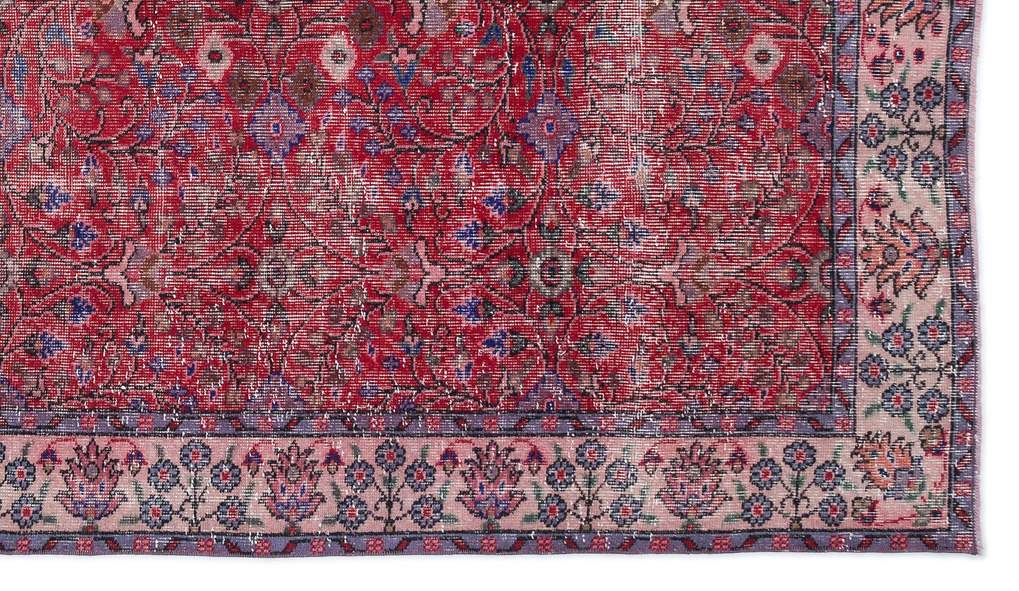 Distressed red traditional rug with a floral medallion pattern and a light pink border featuring blue and purple motifs.