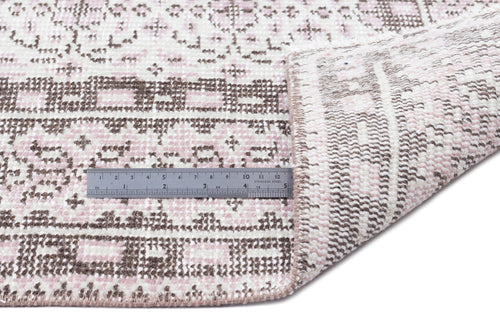 Load image 1 in gallery view. Pink and brown geometric patterned rug with a folded corner and a metal ruler for scale on a white background.