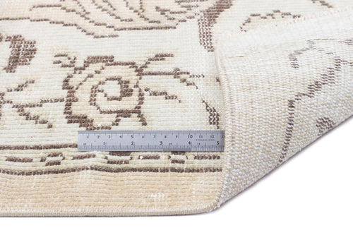 Load image 1 in gallery view. Cream and brown floral patterned rug with a folded corner and a metal ruler for scale on a white background.