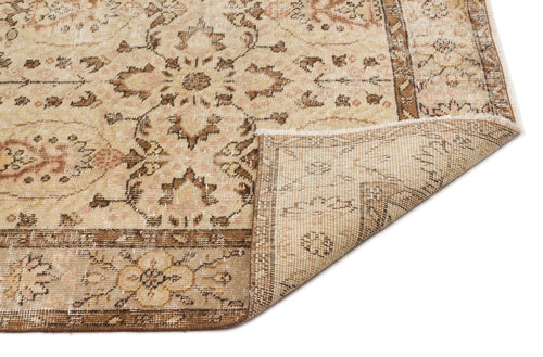 Load image 1 in gallery view. Beige and brown vintage-style rug with a floral medallion pattern and a folded corner showing the woven backing.