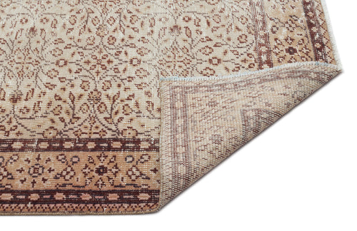 Load image 1 in gallery view. Beige and brown vintage-style rug with a floral pattern and a folded corner showing the woven backing.
