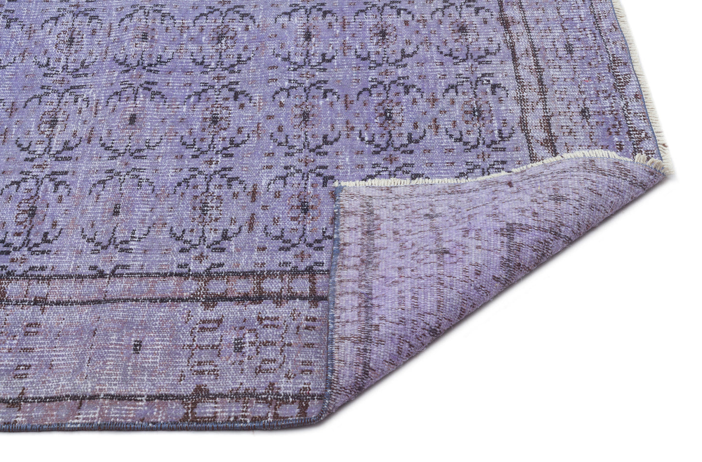 Lavender and charcoal distressed rug with a repeating floral medallion pattern and a folded corner showing the backing.
