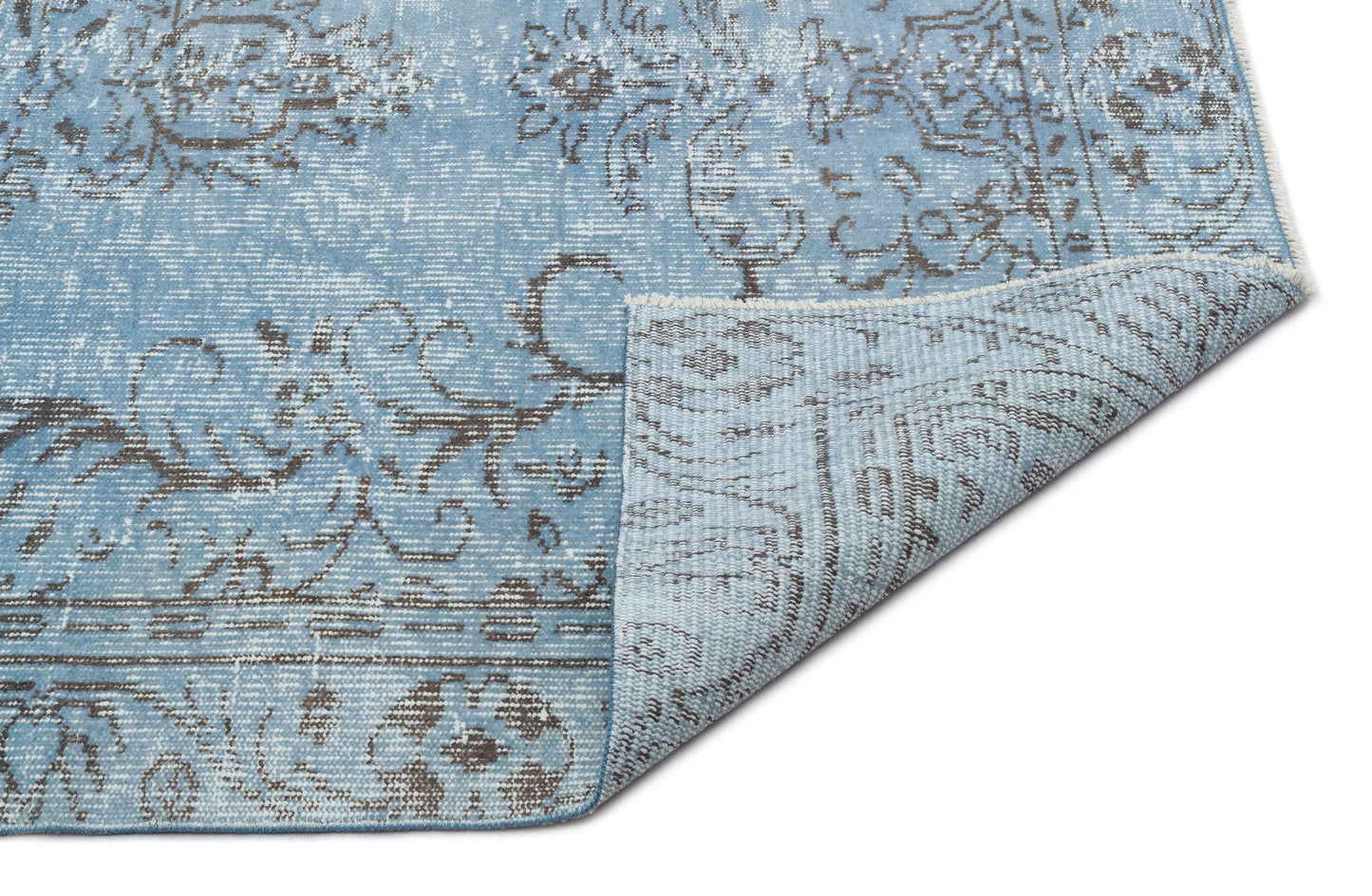 Light blue and grey distressed rug with a traditional floral medallion pattern, shown with a corner folded over.