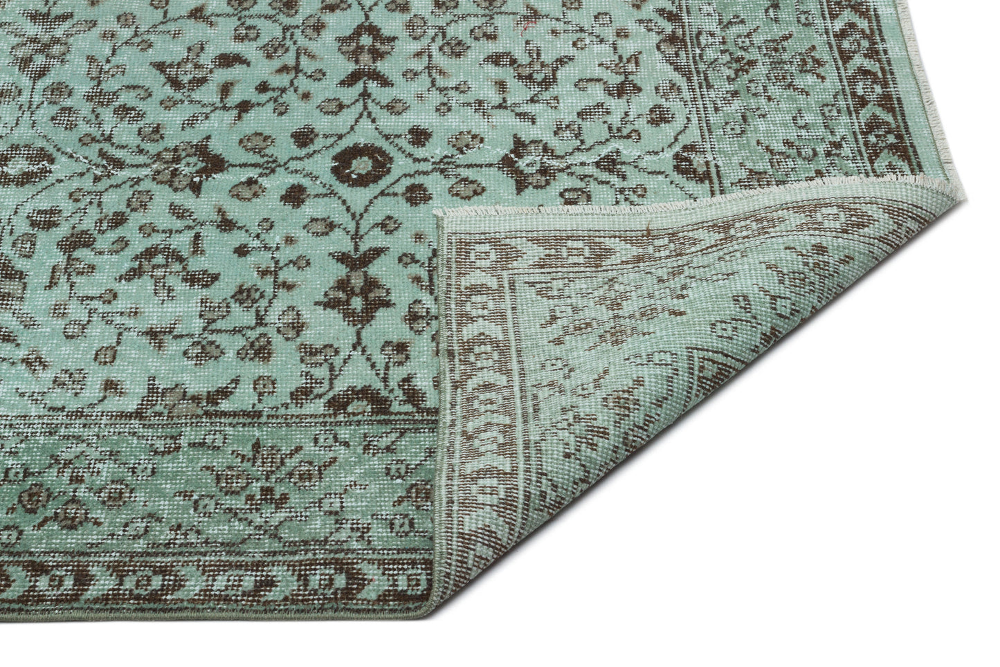 Mint green and brown traditional rug with a floral medallion pattern and a folded corner, isolated on white.
