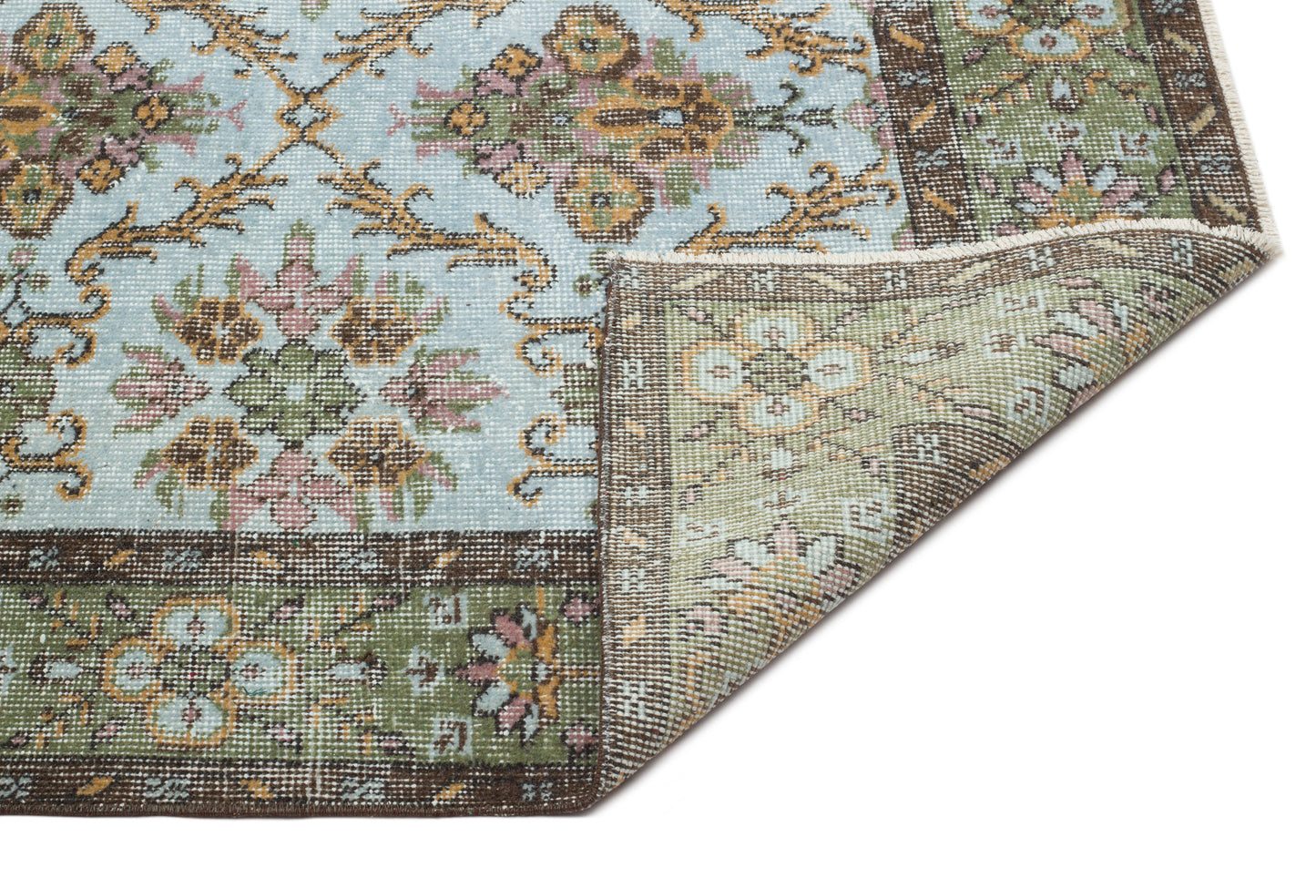 Light blue and green traditional rug with a floral medallion pattern and a folded corner showing the underside.