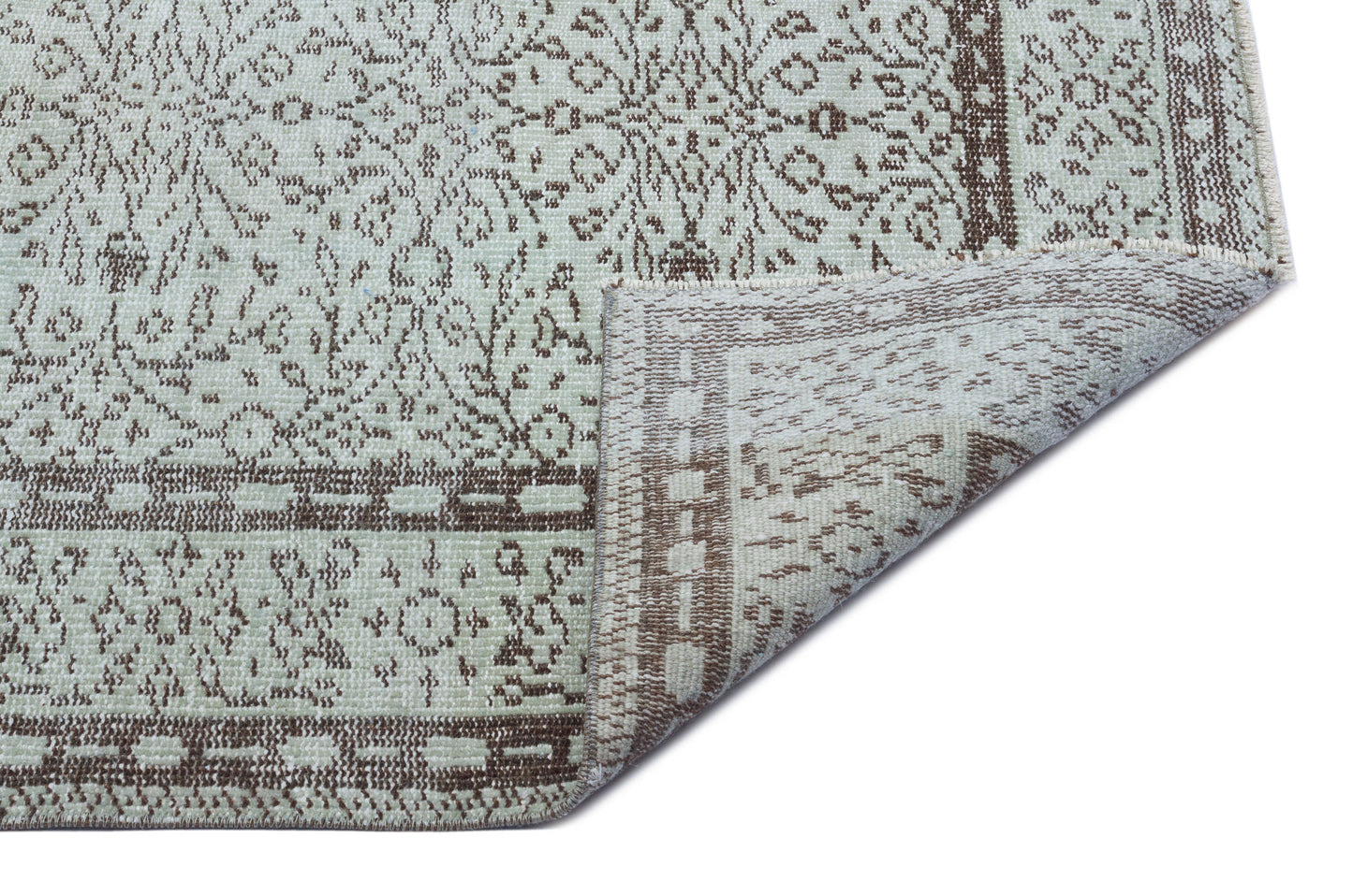 Light green and brown traditional rug with a floral medallion pattern, shown with a corner folded over on white.