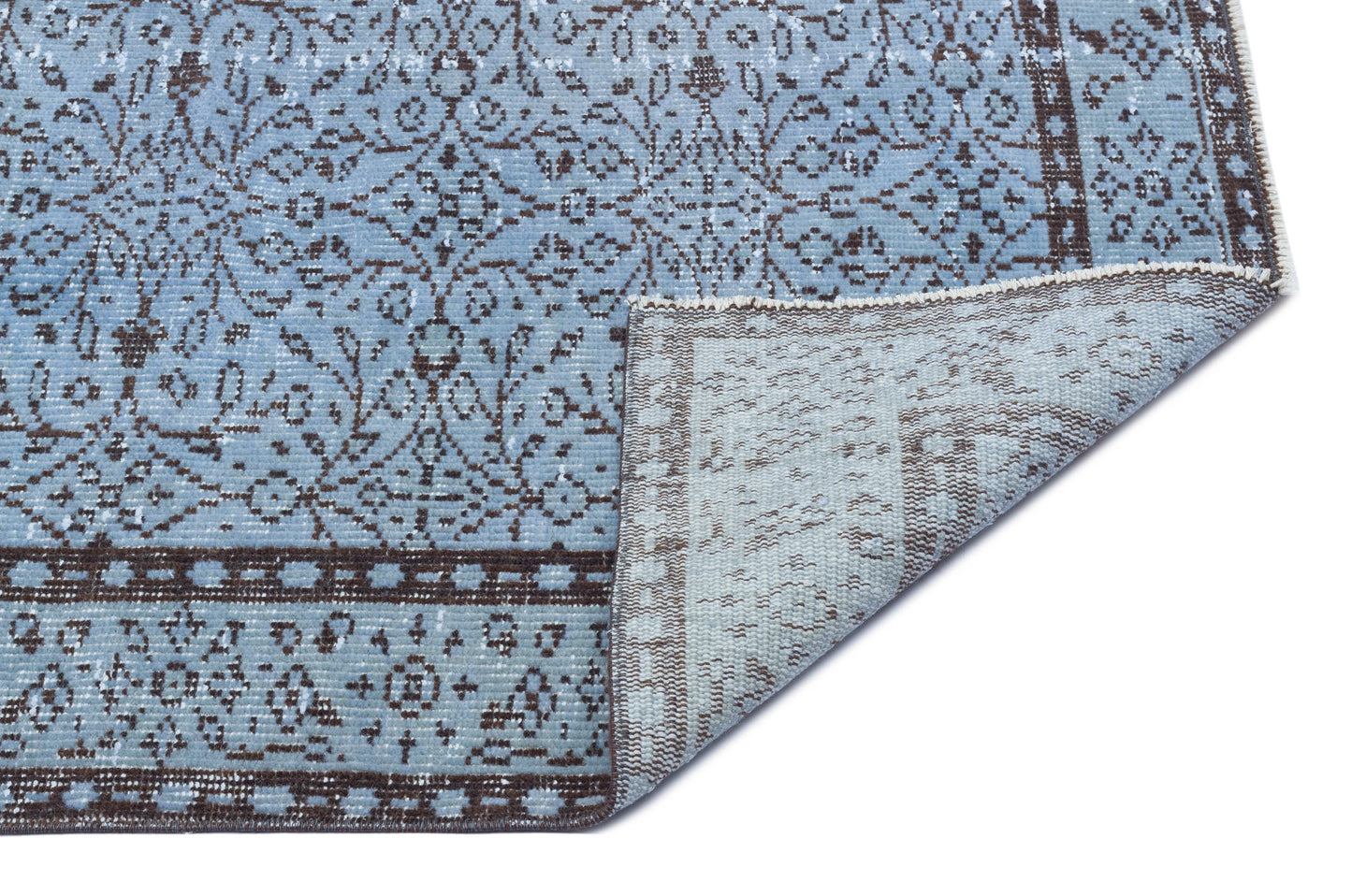 Light blue and brown distressed rug with a traditional floral medallion pattern, shown with a corner folded over.