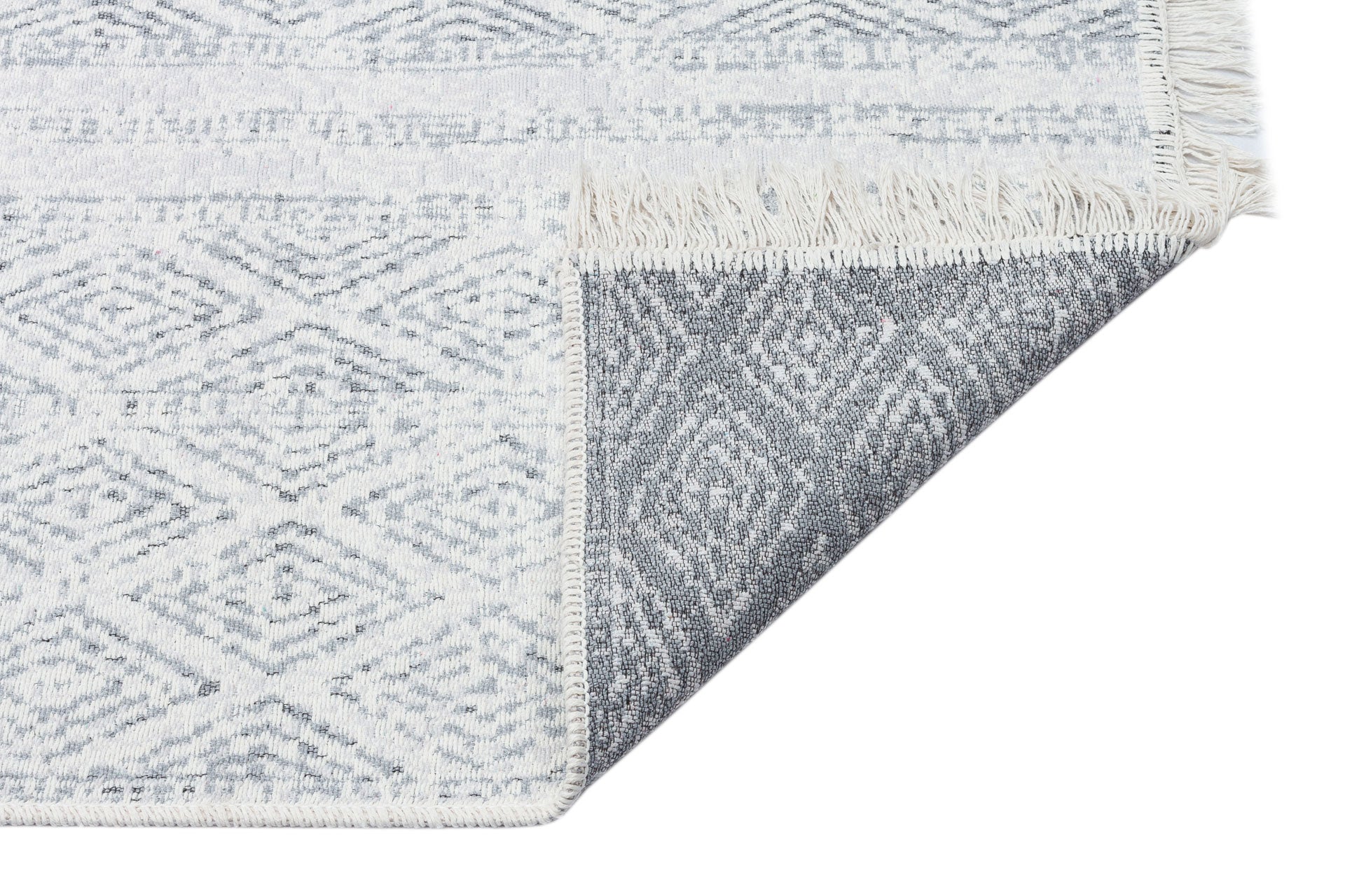 A close-up of the Modern Mist - Washable Double-Sided Kilims - AR01 shows its fringed edges and geometric diamond pattern, with one corner flipped to reveal the gray underside for a sleek, modern look.