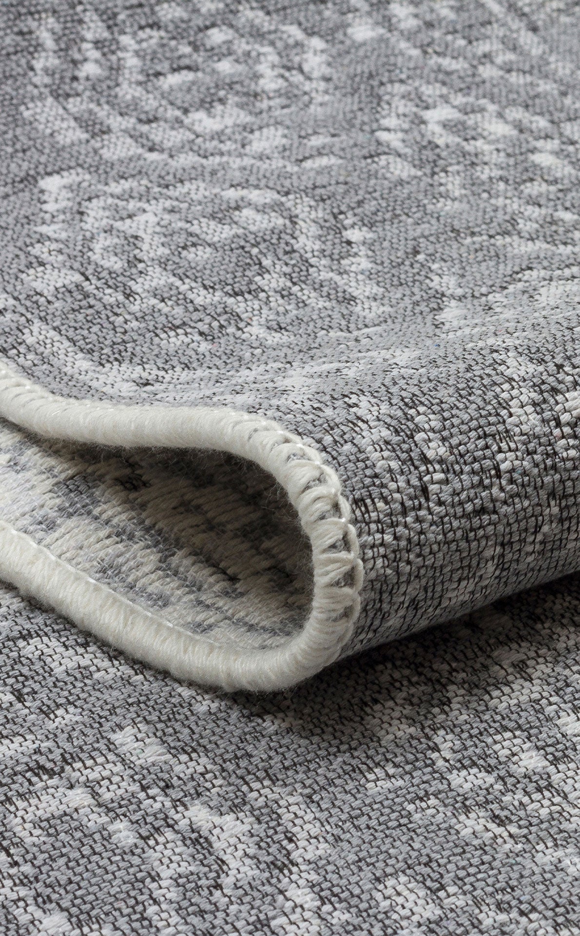 Close-up of the Modern Mist - Washable Double-Sided Kilims - AR01, a folded grey rug with a subtle geometric pattern and visible edge stitching, highlighting its contemporary style and quality craftsmanship.