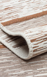A close-up of the Calm Thread - Washable Double-Sided Kilims - AR27, folded at the edge and displaying a textured pattern in beige, brown, and white stripes—ideal as a neutral area rug for any room.