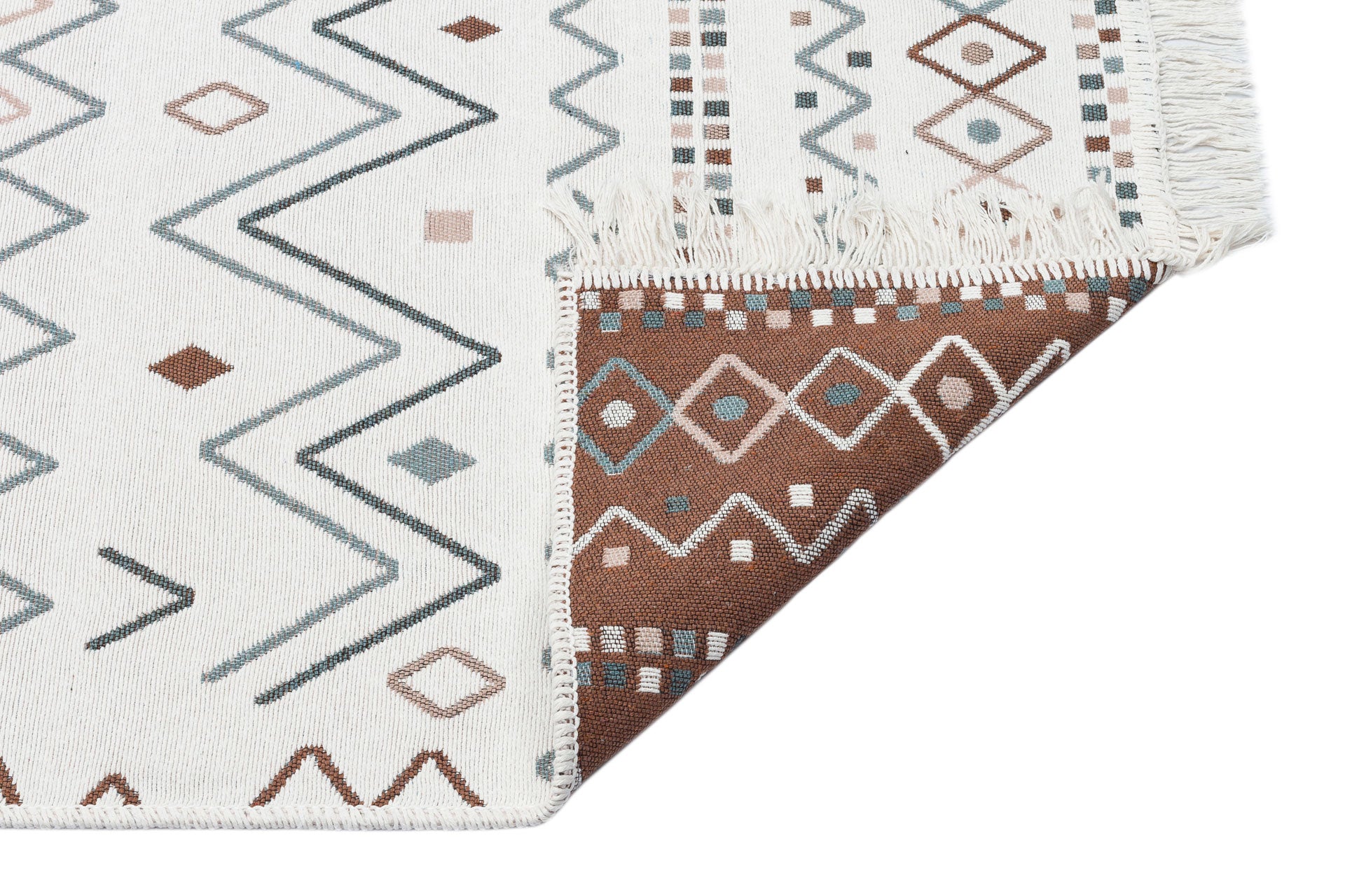 A corner of the Sand Horizon - Washable Double-Sided Kilims - AR05 shows geometric patterns in brown, blue, and beige; one edge is flipped to reveal the darker reverse side and visible fringes.