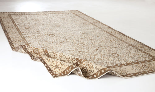 Load image 1 in gallery view. Beige and brown traditional rug with a floral medallion pattern and a folded corner on a white background.
