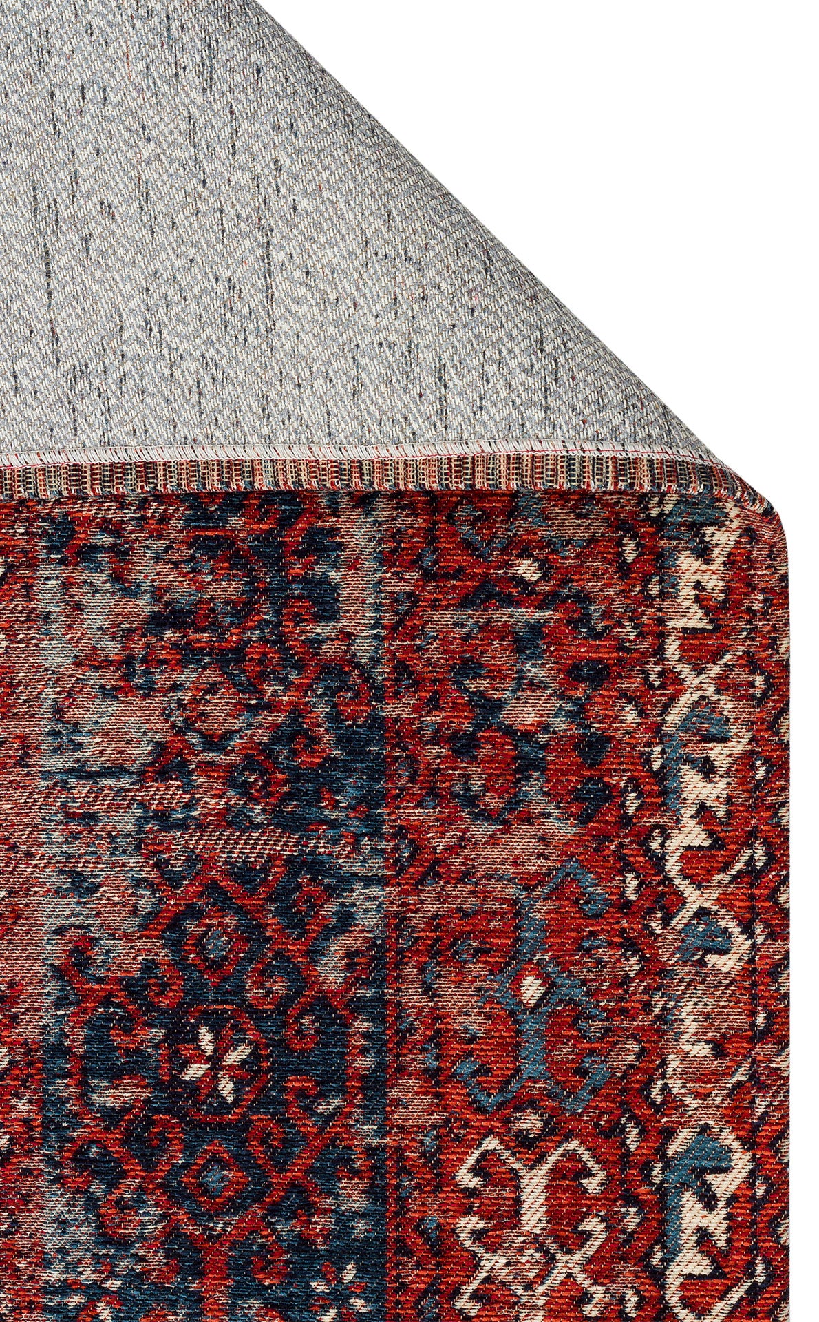 A close-up of the Heritage Blend - Washable Kilims - AND02 rug shows its red and navy chenille polyester pattern and decorative border. The corner is flipped to display a gray, dotted non-slip backing—an allergy-conscious choice.