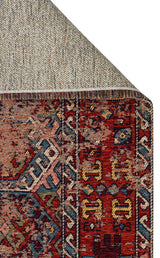 Close-up of a corner of the Nomad Spirit - Washable Kilims - AND03 rug, featuring geometric and floral patterns in red, blue, gold, and cream, with its underside folded to reveal the textured backing.