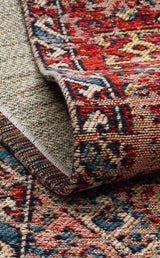 A close-up of the Nomad Spirit - Washable Kilims - AND03 rug highlights its intricate red, blue, and cream flatwoven patterns, with the edge folded to showcase the detailed texture and reversible design