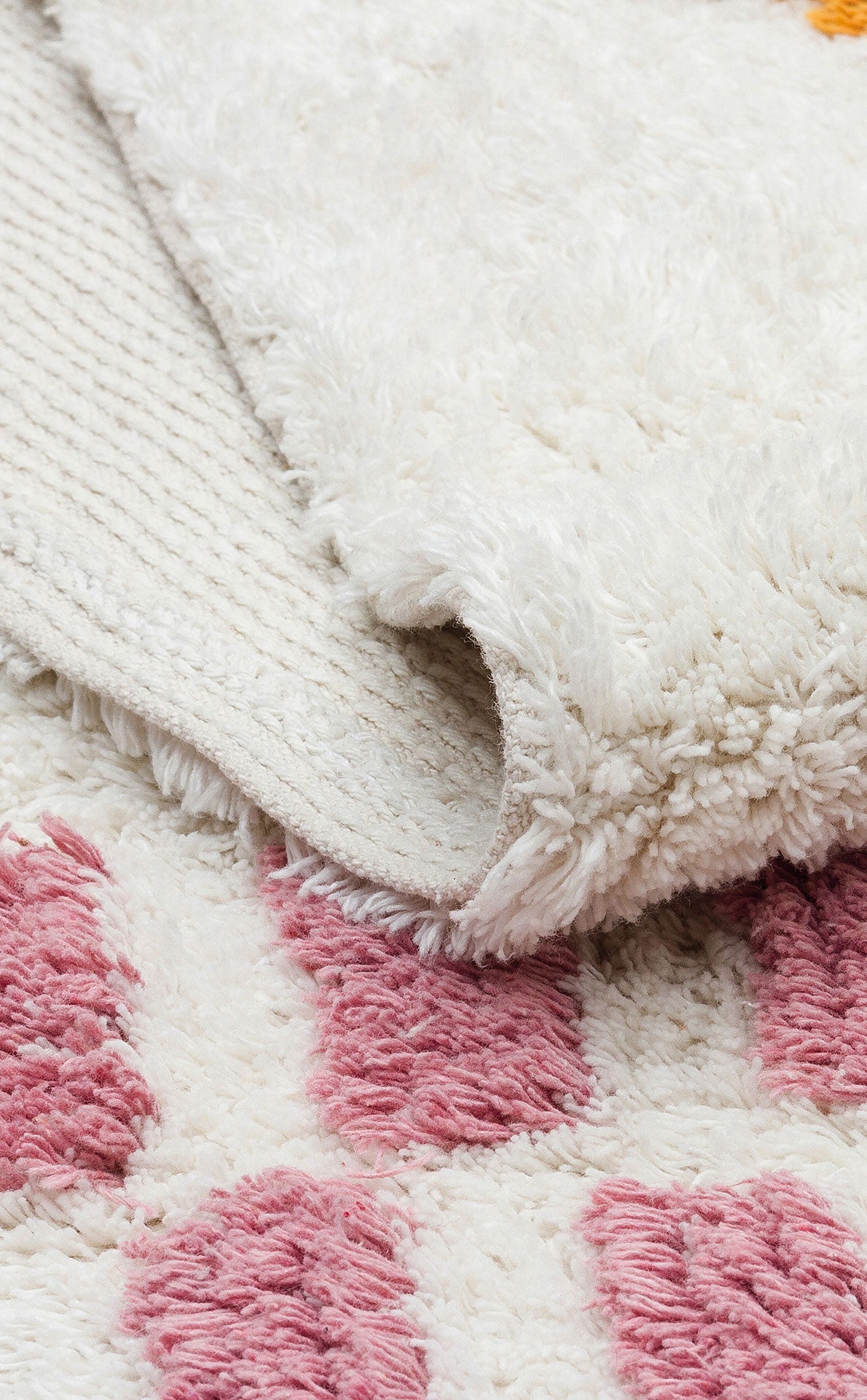 A close-up of the Nursery Nest - Washable Shaggy - CBN04 rug shows its plush, textured underside, with a pink geometric pattern on a soft white background—perfect for nursery decor.