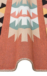 A close-up of the Artisan Mesh - Washable Double-Sided Kilims - AR39, a multicolour recycled cotton rug in orange, beige, black, green, and white geometric patterns, draped over a curve to showcase its texture and design.