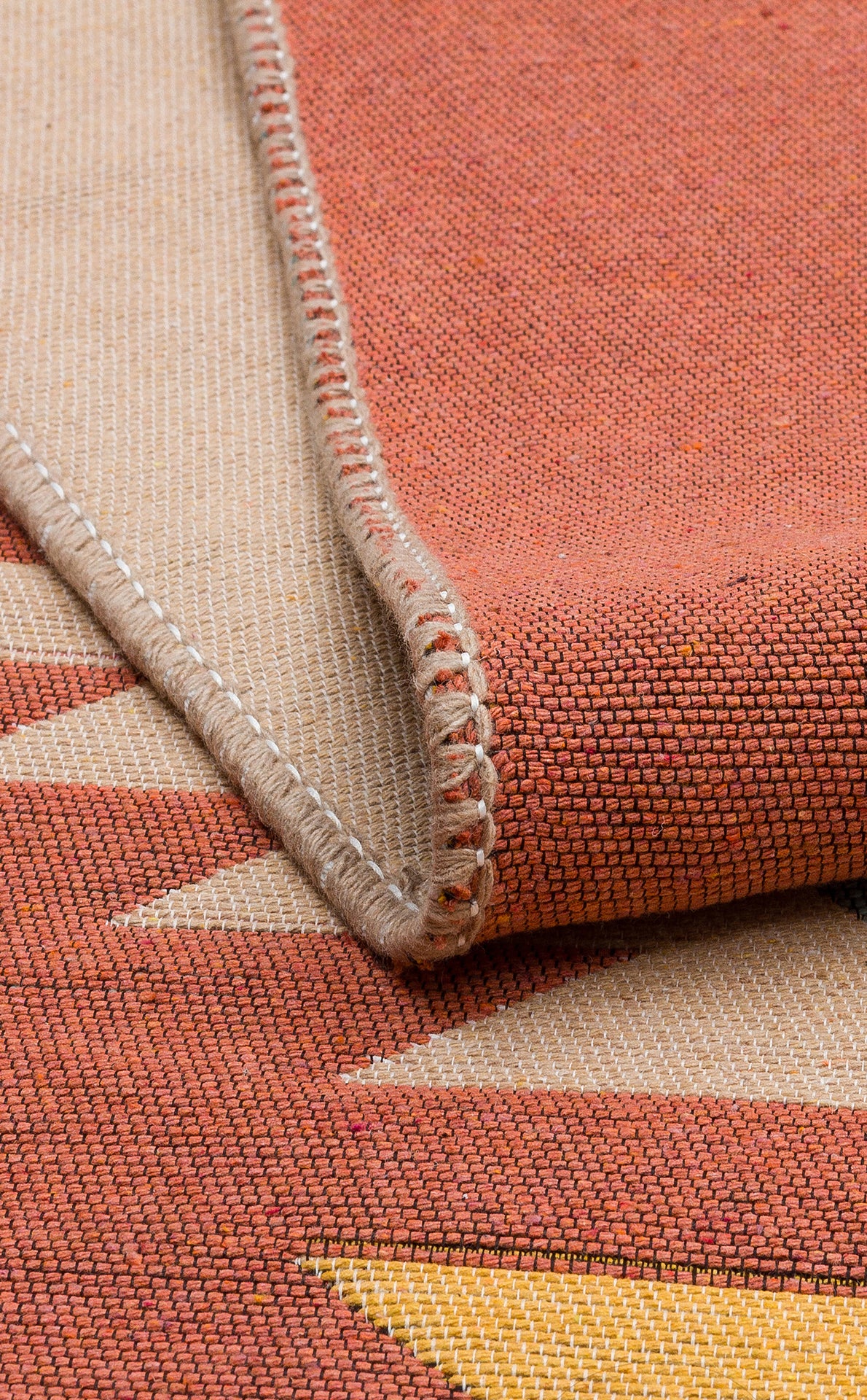 Close-up of the Artisan Mesh - Washable Double-Sided Kilims - AR39, a recycled cotton rug with a red, beige, and yellow geometric pattern. The folded edge shows detailed hem stitching and highlights its textured, tightly woven surface.