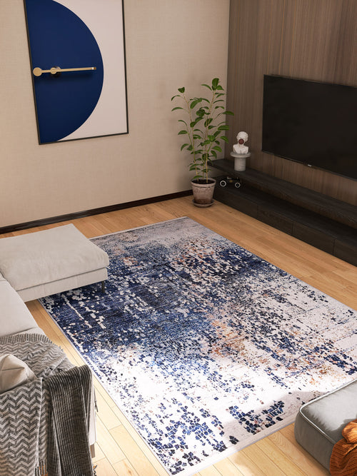 Load image 1 in gallery view. A modern living room featuring the Abstract Atmosphere - Washable Rug - JR834 (Custom Size) in blue and white, ideal for high-traffic areas, a gray sectional sofa, potted plant, wall-mounted TV, and geometric blue and gold artwork.