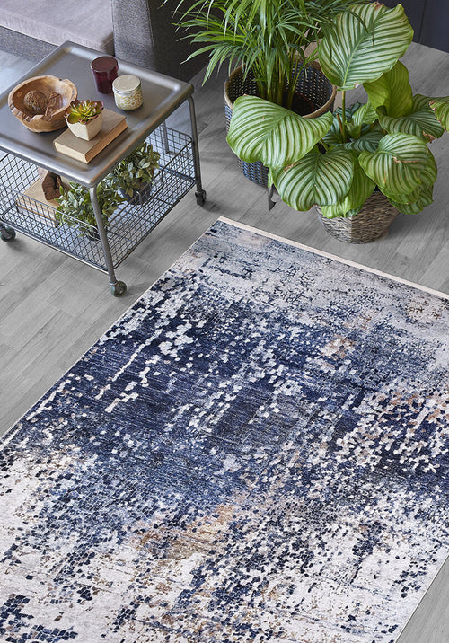 Load image 1 in gallery view. A living room corner with the Abstract Atmosphere - Washable Rug - JR834 (Custom Size) in blue on a light wood floor. A metal side table holds decor and a plant, while two large green potted plants bring fresh style nearby.