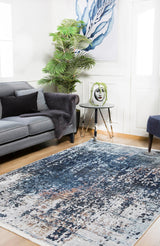 A modern living room with a gray sofa, black pillow, potted plant, round side table with a decorative face vase, abstract blue wall art, and the Abstract Atmosphere - Washable Rug - JR834 (Custom Size), ideal for high-traffic areas.