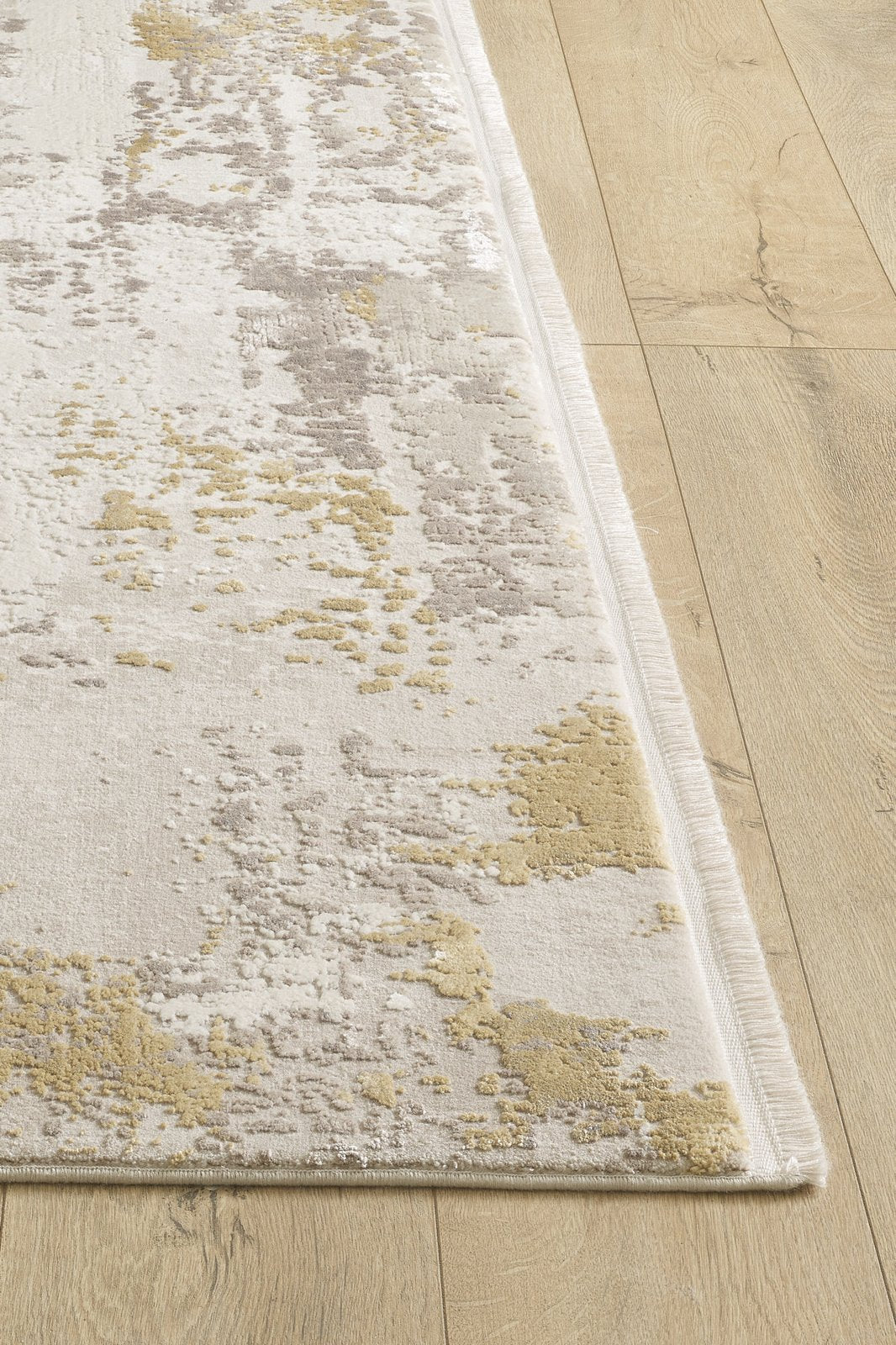 A close-up of the Abstract Blitz Premium Rug - Gold - M658F showcases its textured abstract pattern in beige, gray, and yellow tones on a light wood floor.
