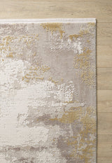 The Abstract Blitz Premium Rug - Gold - M658F features a machine-made abstract design in beige, ivory, gray, and gold with irregular textured patches, bringing contemporary style to a light wooden floor.