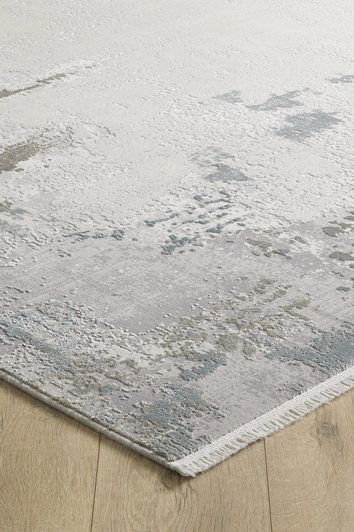 Load image 1 in gallery view. The Abstract Blitz Premium Rug - Silver - M658D features a modern, machine-made abstract pattern in muted gray, beige, and blue with short white fringe, shown here on a light wood floor.