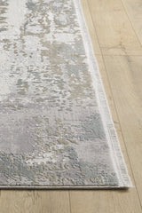 A close-up of the Abstract Blitz Premium Rug - Silver - M658D shows its modern abstract pattern in gray, cream, and light blue on a light wood floor. This machine-made rug features a thin fringe along the edge for added detail.