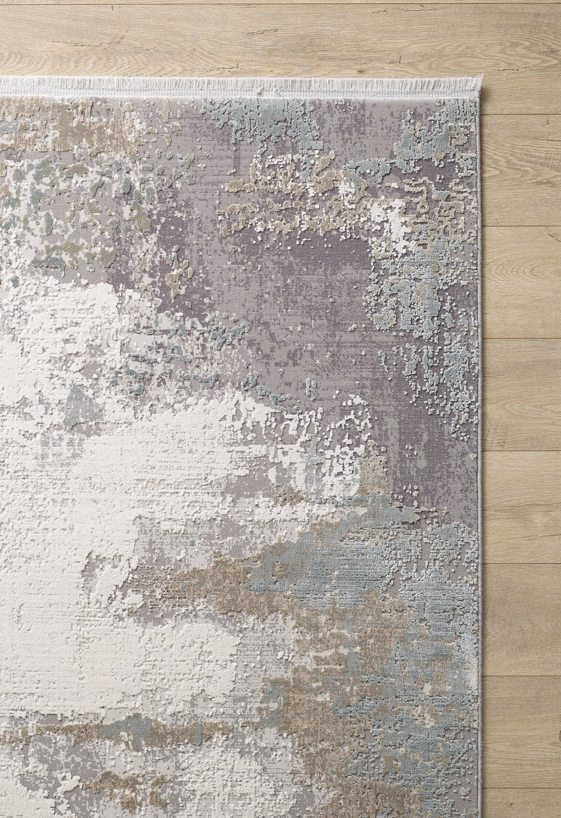 The Abstract Blitz Premium Rug - Silver - M658D, a modern machine-made rug with an abstract gray, white, beige, and pale blue pattern, features subtle texture and short fringe on one edge for a contemporary look atop the light wooden floor.