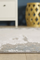 A close-up of the Abstract Blitz Premium Rug - Silver - M658D on a wooden floor, with part of a white cabinet and a decorative gold stool in the background.