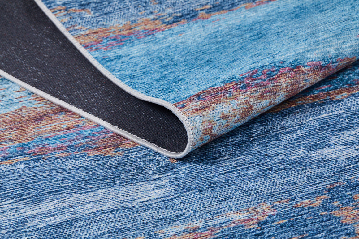 A close-up of the Abstract Elegance - Machine-Washable Rug JR87 (Custom Size) in blue shows its multicolored textures, a flipped corner revealing the black underside, and detailed edge stitching—ideal for high-traffic spaces.