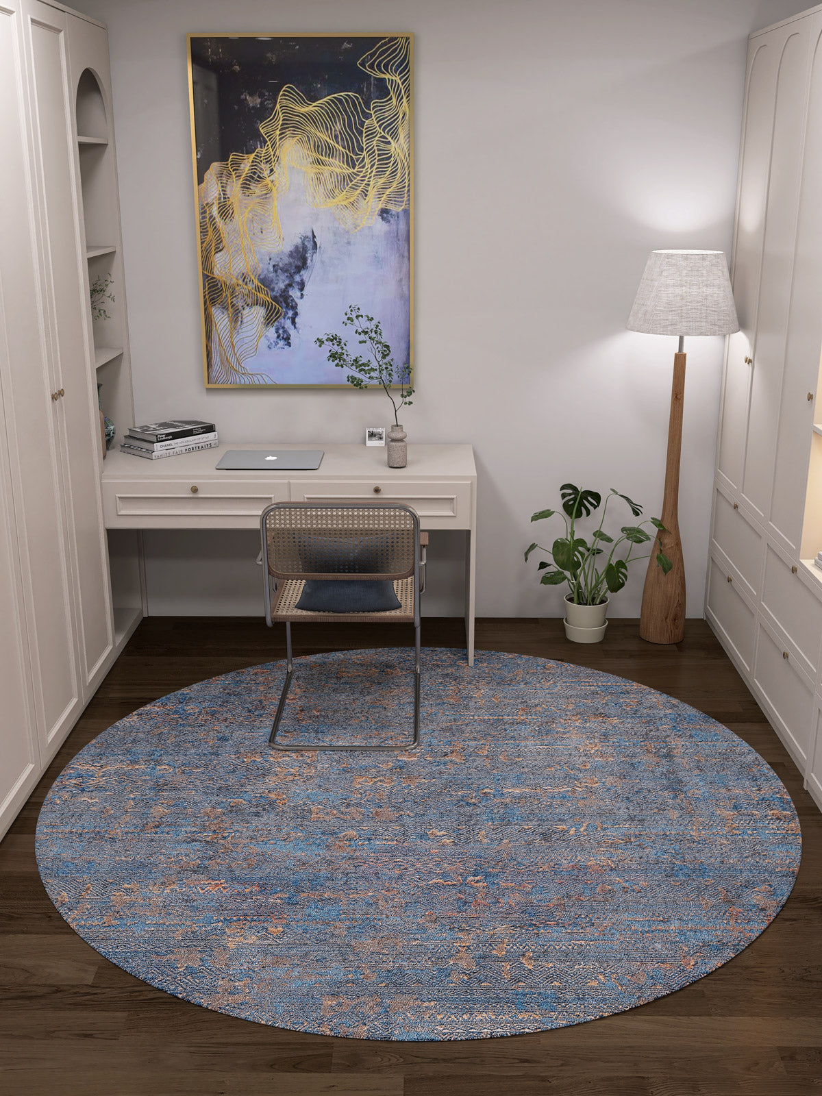 A modern home office features a white desk, rattan chair, and the Abstract Harmony - Machine-Washable Rug JR1882 (Custom Size)—ideal for high-traffic areas. A tall lamp and plant stand right; gold and blue abstract art hangs above built-in white shelves.