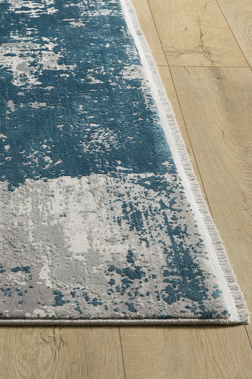 Load image 1 in gallery view. A close-up of the Abstracta Blue Premium Rug - 1004F, a machine-made rectangular rug with blue and gray abstract patterns, short white fringe, shown on a light wood floor.