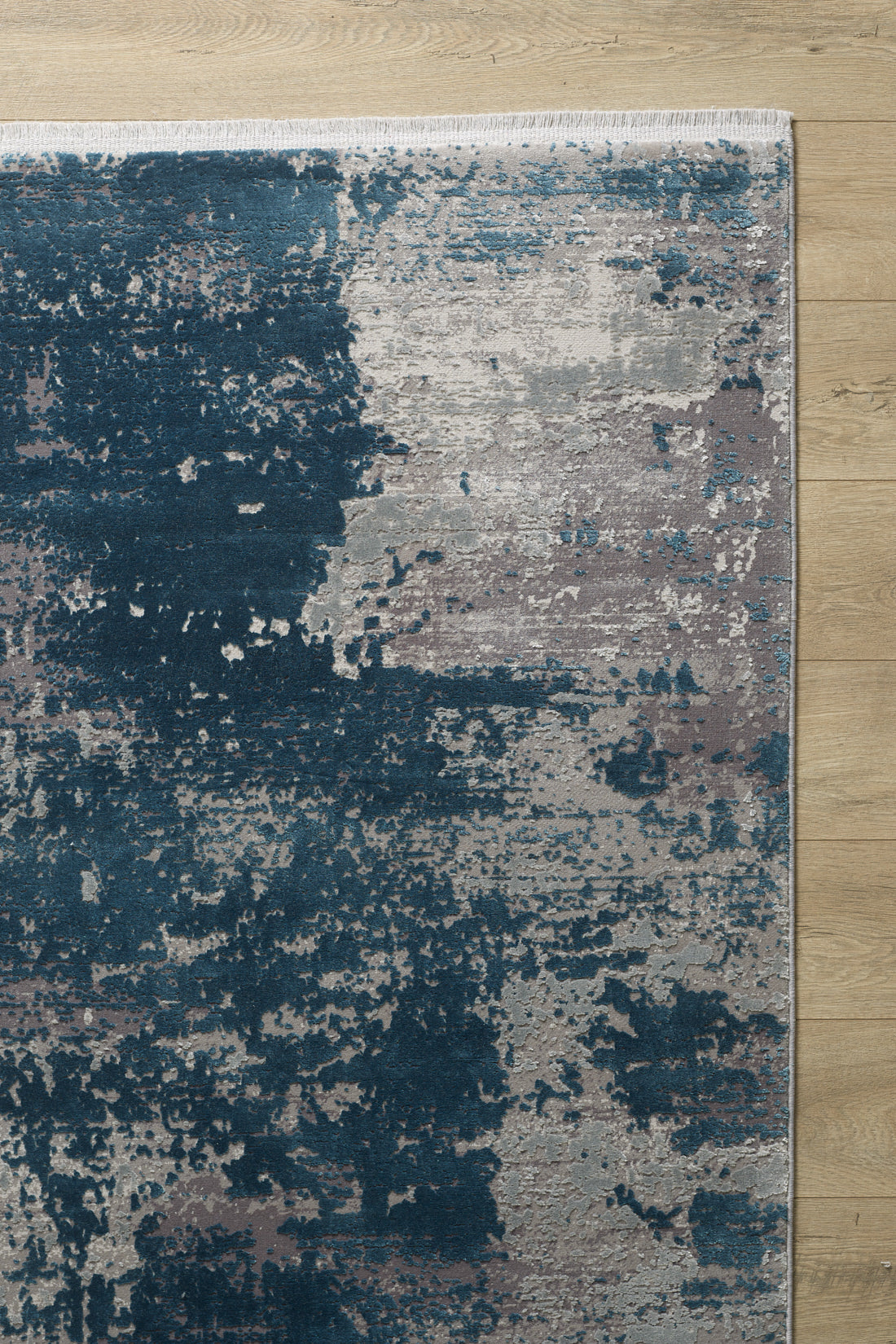 The Abstracta Blue Premium Rug - 1004F features a textured, painterly pattern in dark blue, light gray, and taupe tones. This machine-made rug is displayed on a light wooden floor.