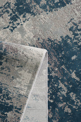 A close-up of the Abstracta Blue Premium Rug - 1004F, a machine-made piece with a folded corner, showcasing an abstract pattern in blue, gray, and beige tones.