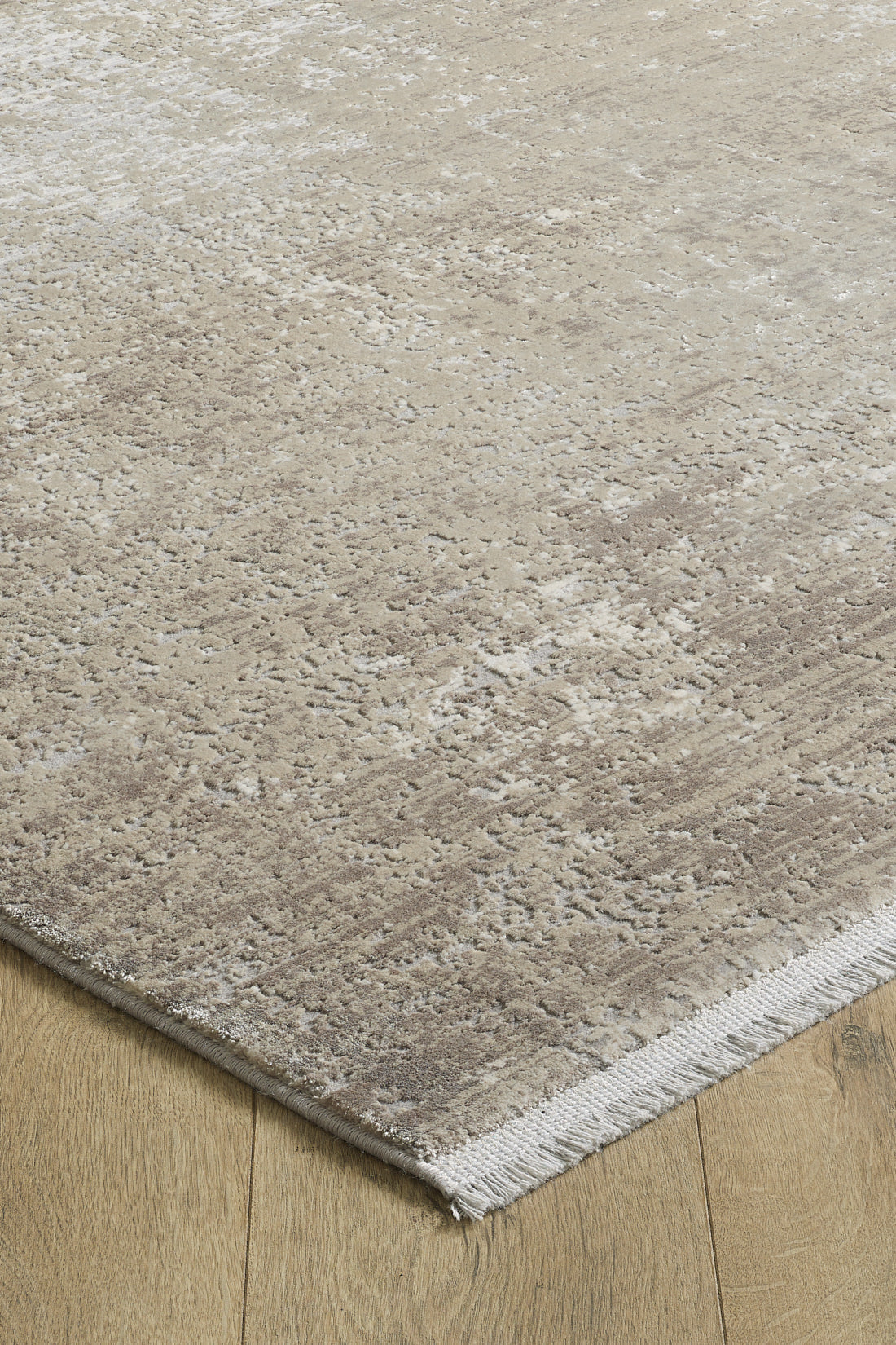 A close-up of the Abstracta Creme Premium Rug - 1004B, featuring a beige and light brown abstract, textured pattern with short fringes, on a light wooden floor. This machine-made rug brings modern elegance to any space.