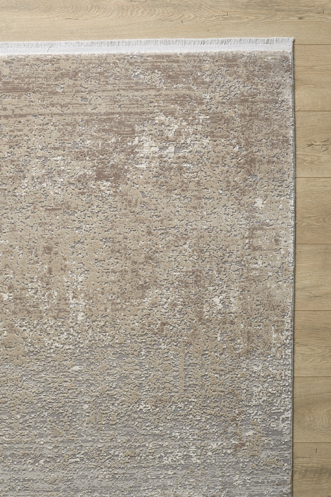 The Abstracta Creme Premium Rug - 1004B, featuring a textured abstract pattern in beige and gray, lies on a light wood floor. Only part of this modern acrylic-viscose rug is visible in the image.
