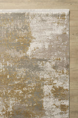 The Abstracta Gold Premium Rug - 1004G, a modern machine-made piece in beige, gold, cream, and gray with a textured, distressed abstract pattern and uneven color patches, is shown on a light wooden floor.